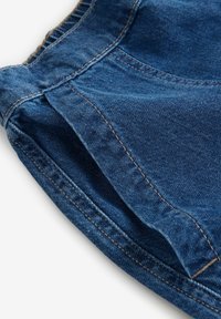 Gros plan sur un tissu en denim bleu montrant des coutures détaillées et une ouverture de poche sur un vêtement.
