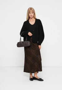 Mustavilla neulecardigan mustan topin päällä, yhdistettynä ruskeaan leopardikuosisessiin maksihameeseen. Pitelee tummaa ruskeaa strukturoitua käsilaukkua, jalassa mustat ballerinat.