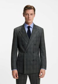 Giacca da suit grigia a quadri doppiopetto, vestibilità su misura, morbida al tatto, con rever a punta, due tasche frontali, abbinata a una camicia azzurra chiara e una cravatta blu navy.