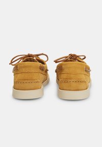 Scarpe in suede gialle con profilo basso, dotate di dettagli in pizzo marrone e suola in gomma beige. La parte posteriore presenta un accento cucito e una finitura liscia.