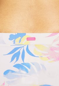 Top de bikini floral multicolorido com padrões azuis, amarelos e rosas sobre um fundo branco; apresenta uma etiqueta rosa da Roxy na frente.