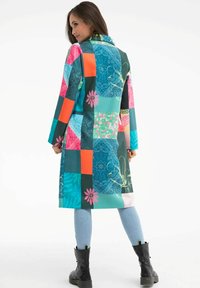 Dlouhý patchworkový kabát v živých barvách, jako je tyrkysová, růžová a oranžová. Vyrobený z hladkého materiálu s květinovými a geometrickými vzory.