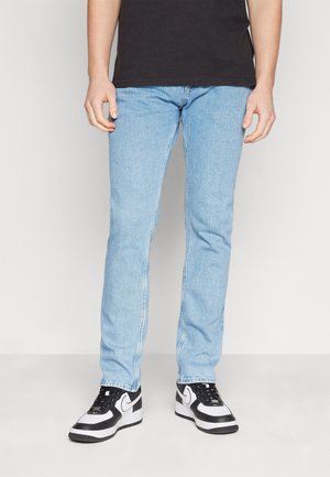 Jeans de mezclilla azul claro con corte recto y costuras visibles. Combinados con zapatillas negras y blancas con un acento de logo.