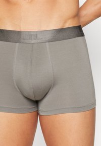 Gray boxer shorts made of soft material with a snug fit. Features a dark elastic waistband with a subtle logo and clean stitching details.