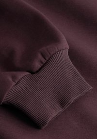 Gros plan d'une manche de sweat-shirt violet foncé avec un poignet côtelé et une texture de tissu douce et lisse.