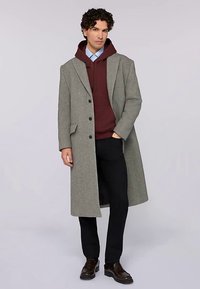 Grå ullrock med förlängt snitt, enkelknäppt fram, kombinerad med en vinröd hoodie, mörka byxor och läderskor.