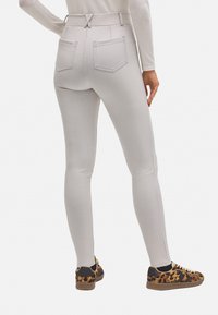 Leggings gris claro con cintura alta, que cuentan con dos bolsillos en la parte trasera y un diseño ajustado, combinados con unas zapatillas de leopardo marrón.