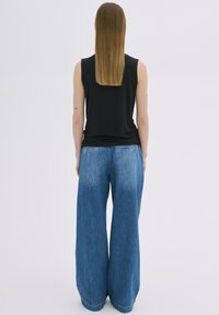 Un haut noir sans manches et un jean en denim bleu clair à jambes larges. Le jean a un délavage léger et possède des poches arrière. Design simple et décontracté.