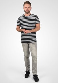 Svart og gråstripete t-skjorte med korte ermer og rund hals, kombinert med lysegrå slim-fit jeans og svarte treningssko.