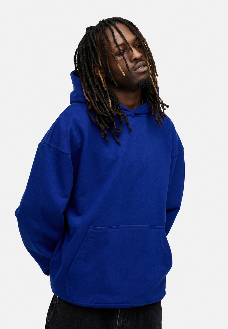 Blaue Kapuzenjacke aus Sweatshirtstoff, mit einer Fronttasche, oversized Passform und Kordelzugkapuze. Texturierte Oberfläche und entspannter Schnitt.