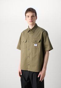 Olive green short-sleeve shirt with pointed collar, two chest pockets, and black buttons. Fabric appears smooth with a relaxed fit.