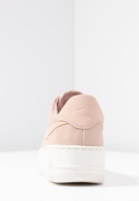 Baskets Nike, tige en daim rose, semelle en caoutchouc blanche, col rembourré, logo en relief au talon, texture lisse, design minimaliste.