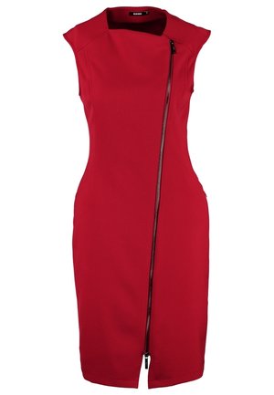 Donna che cammina indossando un abito rosso senza maniche con cerniera diagonale e stivaletti neri con tacco, che tiene una borsa nera da sera.