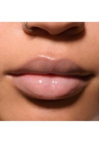 Nahaufnahme von glatten, gut definierten Lippen mit einem glänzenden, durchsichtigen Finish in einem sanften Rosaton. Enthält einen kleinen silbernen Ring im Nasenloch.