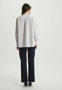 Chemise à rayures en tissu léger, à manches longues, avec un pli dans le dos ; assortie à un jean noir et droit et des escarpins noirs.