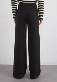 Zwarte wijde broek met hoge taille, gladde textuur en details van een achterzak, gecombineerd met een gestreepte lange mouw top.