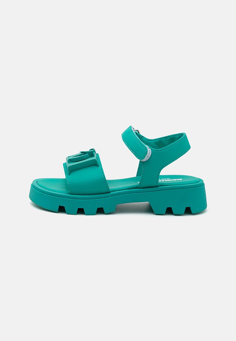 Teal plastsandaler med kraftiga, texturerade sulor. Har två breda remmar och justerbar ankelrem med silverdetaljer. Platt sula.