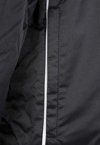 Black jacket fabric with visible stitching and a vertical reflective white strip along a seam.