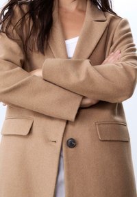 Beige Wollmischungsmantel mit Reverskragen, einer einzelnen schwarzen Knopfschließe und vorderen Taschen. Besitzt eine weiche Textur und einen maßgeschneiderten Schnitt.