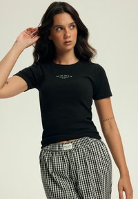 Czarny T-shirt z krótkim rękawem o obcisłym kroju z małym białym napisem na piersi. Połączony z czarno-białymi spodniami w kratę.