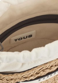 Borsa in fibra naturale con una texture intrecciata, interno beige, zip nera e un'etichetta bianca con la scritta "TOUS". Forma morbida e arrotondata.
