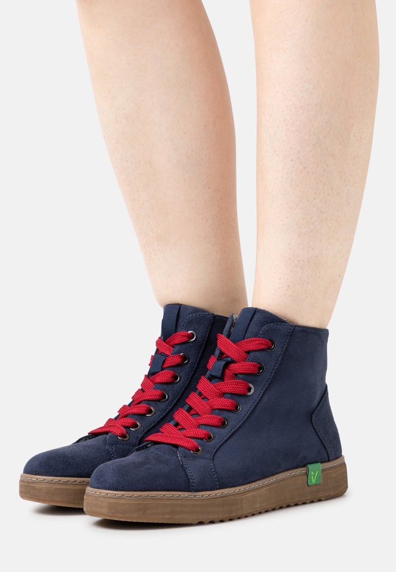 High-top sneakers in navy suede with red laces. Rubber sole, rounded toe, green logo accent on the side. Texture appears soft and durable.