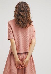 Pudrowa różowa dwuczęściowa stylizacja składająca się z teksturowanej bluzki z krótkim rękawem oraz dopasowanej spódnicy o wysokim stanie, zebranej w talii za pomocą sznurka.