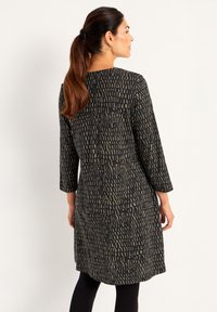 Robe à manches longues noire avec un motif géométrique beige. Confectionnée en tissu doux avec une coupe décontractée et un col rond.
