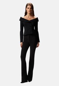 Blazer nero con scollo a barca e design aderente; presenta due bottoni, maniche lunghe e tessuto liscio; abbinato a pantaloni svasati coordinati.