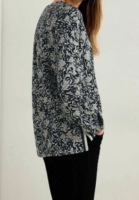 Long-sleeve top featuring a gray and black abstract leaf pattern, with a relaxed fit and side slits for ease of movement.