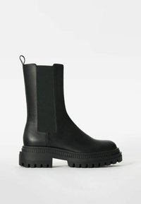 Bota de tobillo de cuero negra con paneles laterales elásticos, suela chunky negra, acabado texturizado y tirador en la parte trasera.