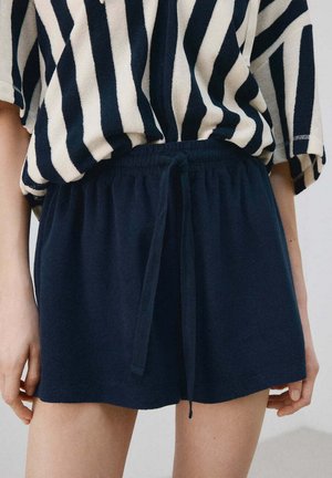 Tmavomodré elastické šortky s predným sťahovaním, nosené s voľným čierno-bielym pruhovaným topom s vertikálnymi pásmi.