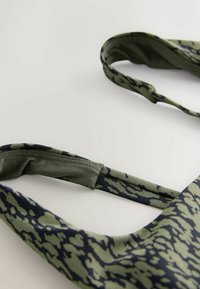 Bretelles réglables en tissu à motif vert et noir avec des parties élastiques sur un fond clair.