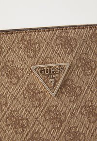 Barna mintás kézitáska struktúrált szintetikus anyagból, ezüst háromszög alakú logoval, rajta "GUESS USA" felirattal.