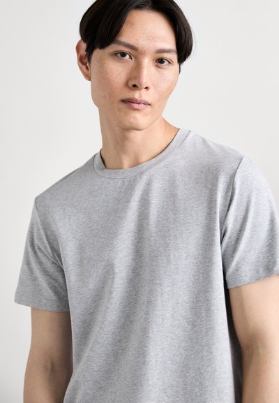 T-shirt en coton gris avec un col rond et des manches courtes. Le tissu a une texture lisse avec un léger motif chiné.