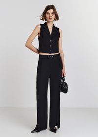 Gilet nero corto con bottoni e tasche abbinato a pantaloni neri a vita alta e a gamba larga con cintura in vita e spacco laterale.