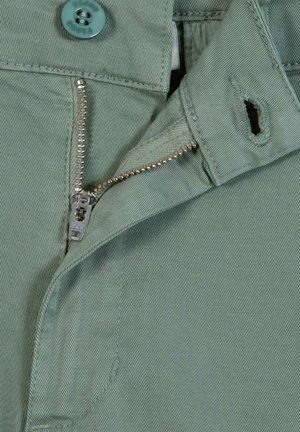 Deels open metalen ritssluiting en knoop op lichtgroene stof, met zichtbare stiksel details op de tailleband van het kledingstuk.