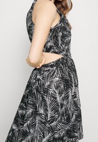 Černobílé šaty bez rukávů s motivem palmových listů, výřezem v pase a splývavou sukní. Hladká, lehká látka.