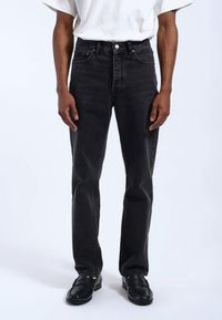 Vaqueros de denim negro con un diseño de pierna recta, estilo de cinco bolsillos y herrajes plateados. Combinados con una camiseta blanca básica y mocasines negros.