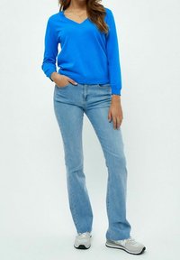 Pull bleu à col en V en tissu léger, associé à un jean bleu clair. Baskets décontractées remarquables avec un design gris et noir.