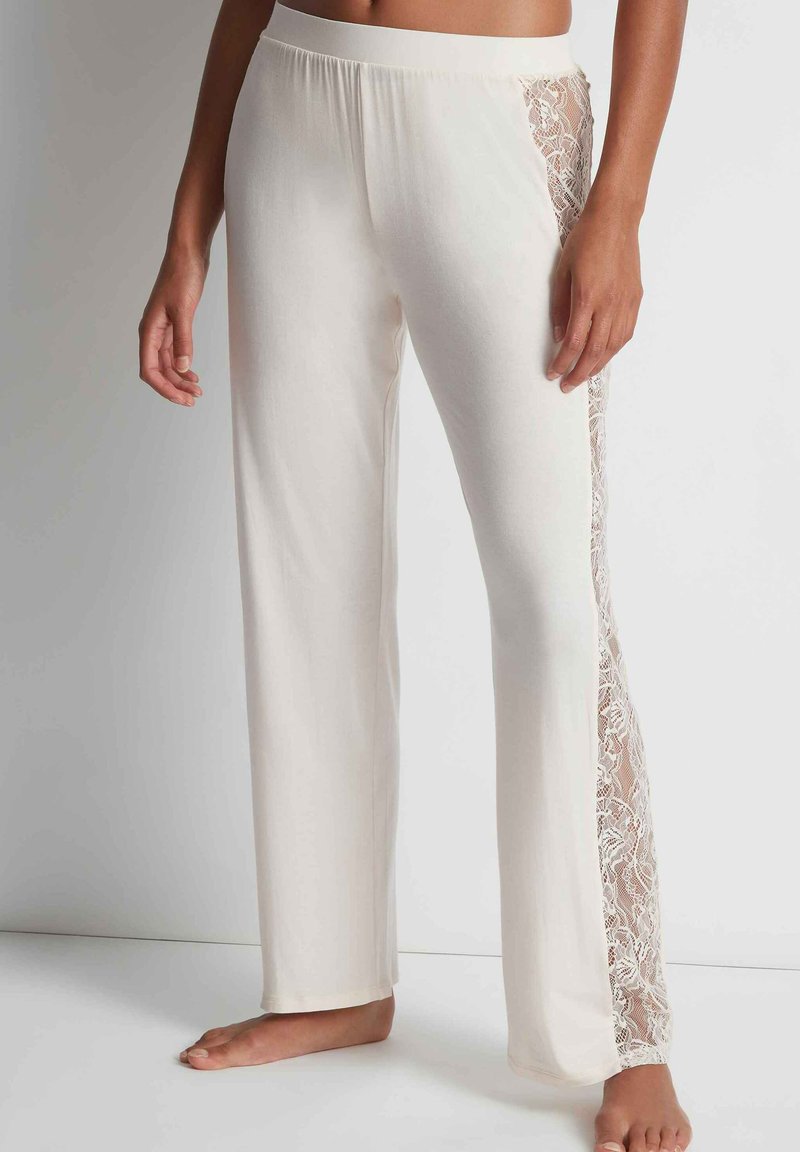 Pantalons de détente en tissu blanc cassé avec une coupe évasée, comportant des panneaux en dentelle transparente sur les côtés et une taille élastique.