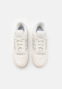 Białe sneakersy z szarymi akcentami, teksturowana skóra i siateczkowa cholewka, perforowany przód, płaskie sznurówki oraz wytłoczone logo na języku.