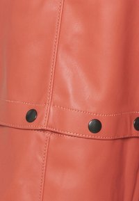 Coral leather fabric featuring a smooth texture, with black metal snap accents and visible stitching detail.