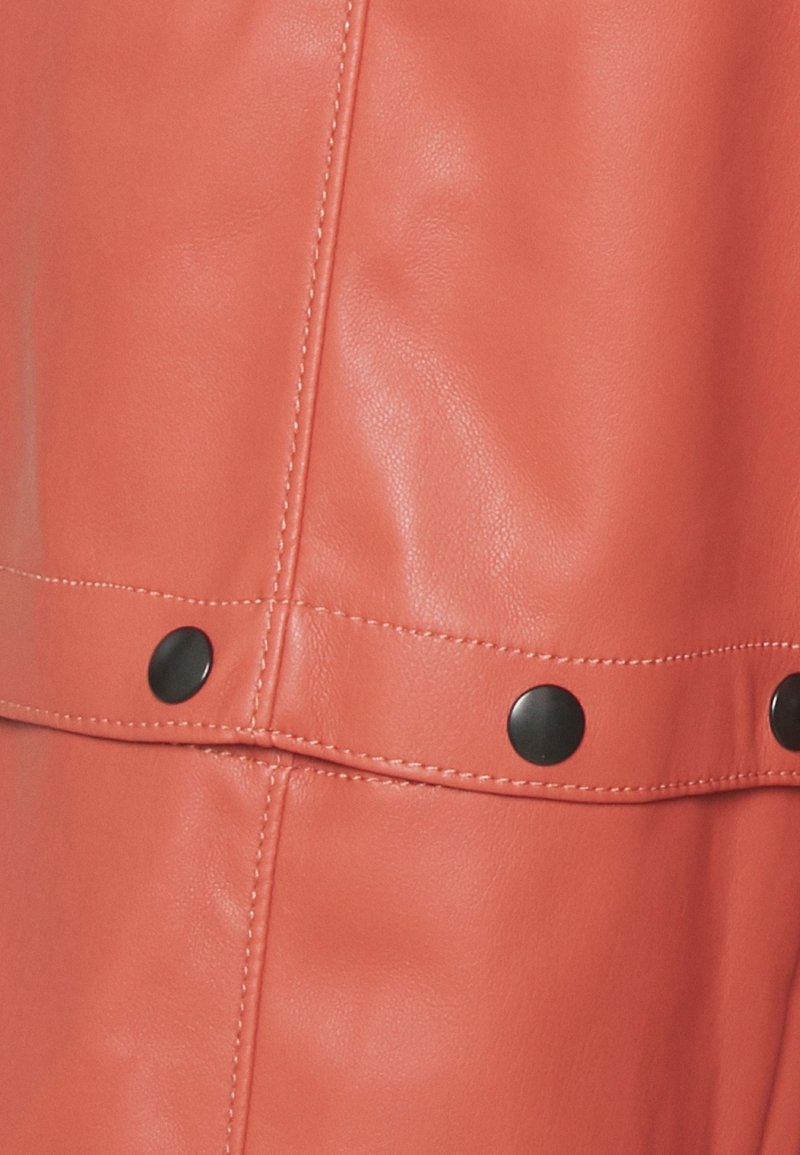 Coral leather fabric featuring a smooth texture, with black metal snap accents and visible stitching detail.