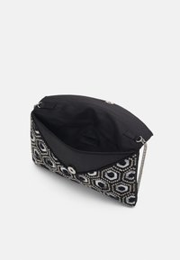 Clutch bag a motivo bianco e nero con design in perline, hardware argento e una tracolla a catena. La patta aperta rivela una fodera interna nera.