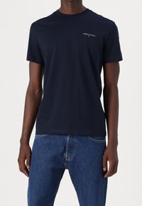 Granatowy bawełniany T-shirt z krótkimi rękawami i okrągłym dekoltem. Małe białe logo "TOMMY JEANS" na lewej piersi.