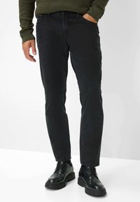 Jeans di denim neri con una vestibilità slim e una sottile trama. Abbinati a scarpe nere con dettagli intricati e una suola spessa.