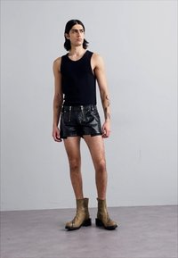Top negru fără mâneci, asortat cu pantaloni scurți metalici negri cu fermoare și cizme elegante până la gleznă de culoare maronie cu toc pătrat.