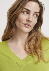 V-Ausschnitt Pullover in leuchtendem Limettengrün, mit gerippter Textur und Strickdetails. Der Stoff wirkt weich und leicht.