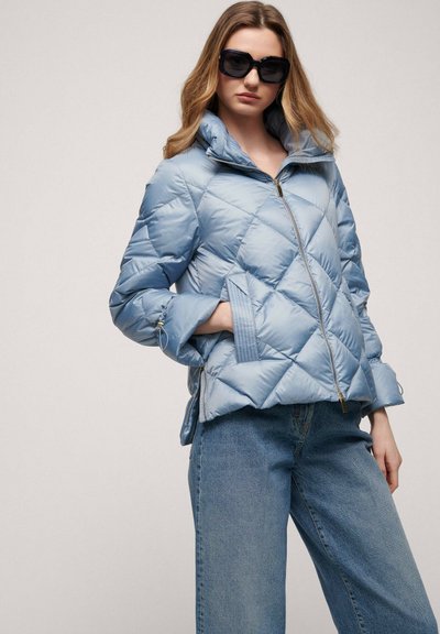 Light blue quilted puffer jacket with a high collar, front zip, and side pockets, paired with wide-leg denim jeans. Smooth, glossy texture.